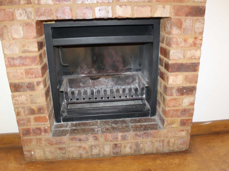 A close-up view of a traditional brick fireplace featuring a built-in metal insert and grate, set within a living area.
