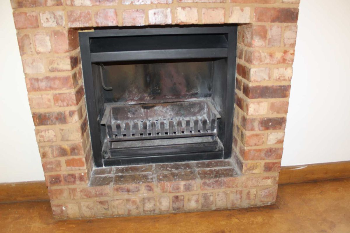 A close-up view of a traditional brick fireplace featuring a built-in metal insert and grate, set within a living area.
