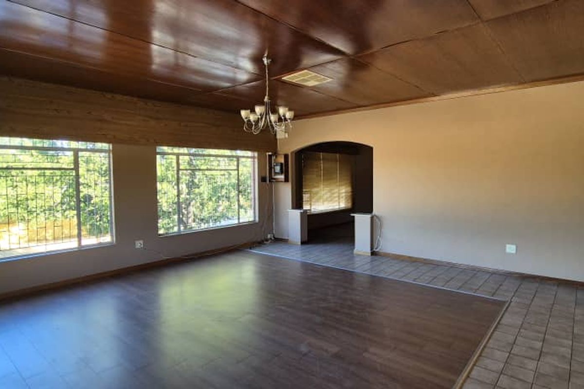 Spacious living area featuring wood-paneled ceilings, large windows with security bars, and a combination of laminate and tiled flooring.