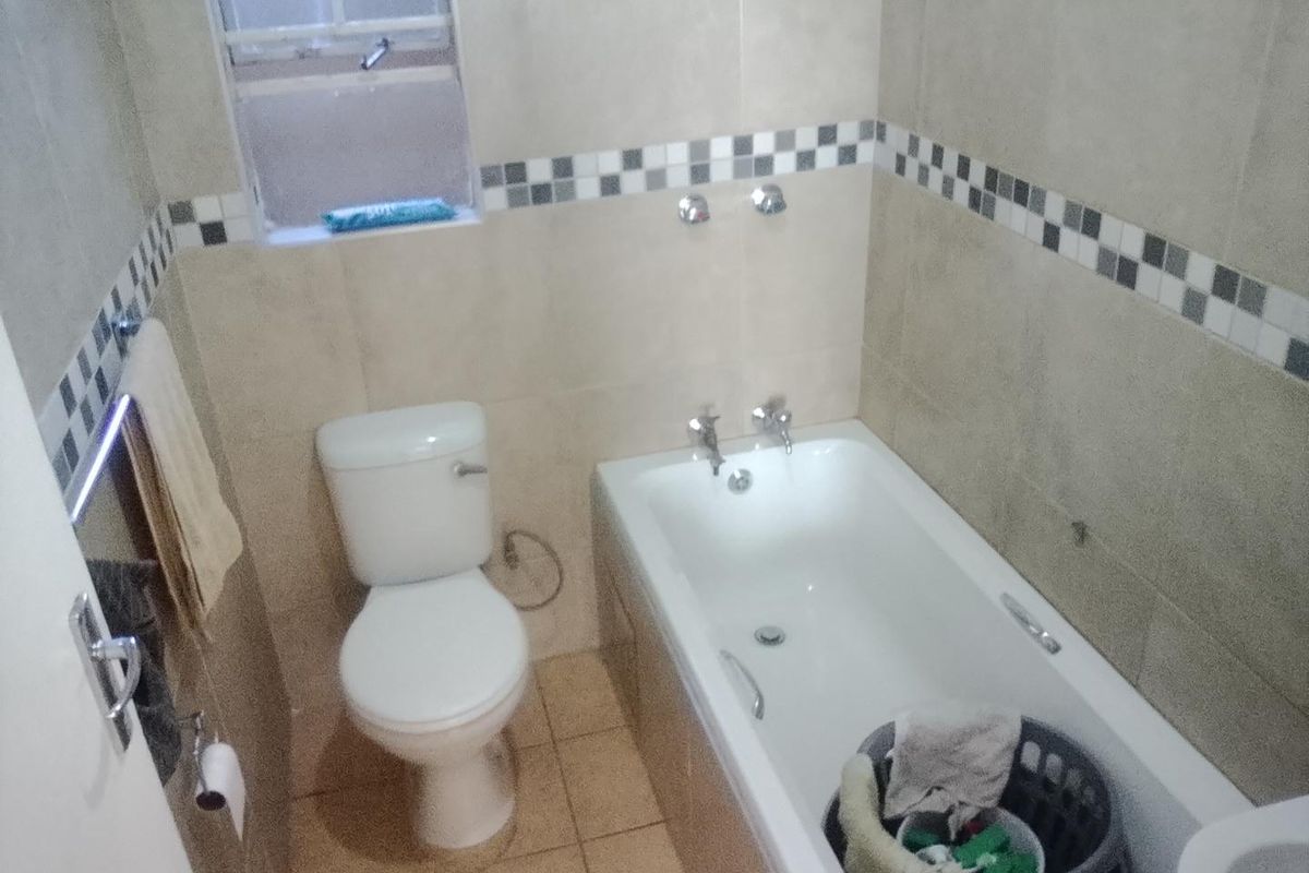 A functional bathroom featuring a standard bathtub, toilet, and neutral wall tiling with a decorative mosaic border.