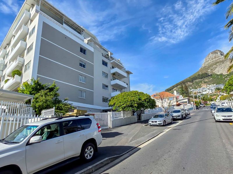 Street-level view of a multi-story apartment building featuring white balconies and grey exterior facade, situated in a coastal residential area.