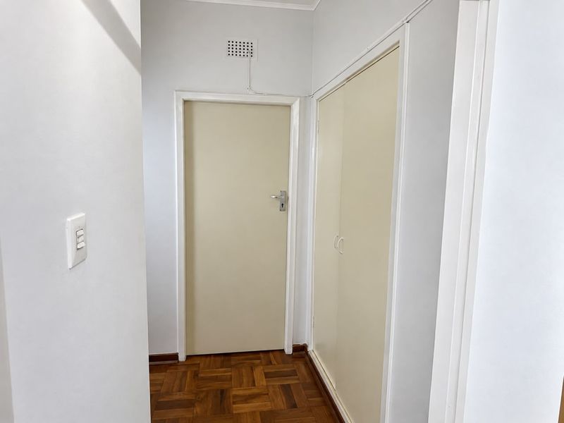 A clean, well-maintained hallway featuring classic parquet flooring and a built-in storage cupboard, providing a functional transition space within the apartment.