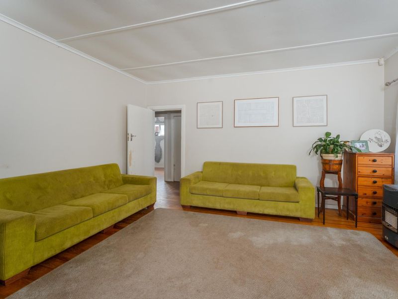 A living room featuring hardwood flooring, a coved ceiling, and a freestanding fireplace, offering a functional space with potential for modernization.