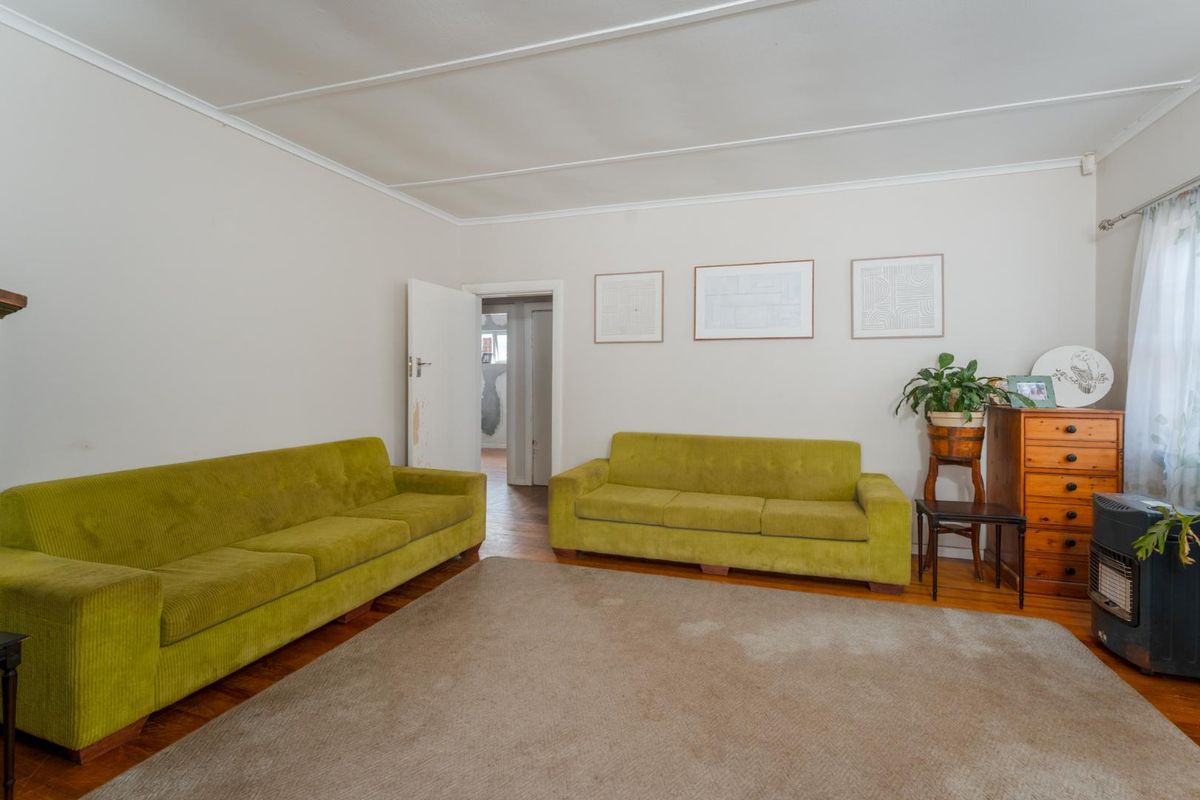 A living room featuring hardwood flooring, a coved ceiling, and a freestanding fireplace, offering a functional space with potential for modernization.