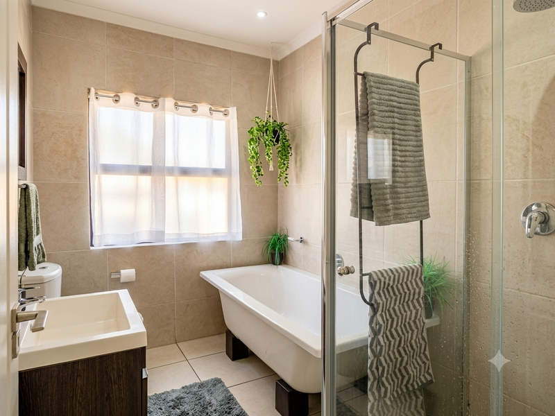 Modern bathroom featuring a freestanding bathtub, glass-enclosed shower, vanity cabinet with basin, and neutral floor-to-ceiling wall tiles.