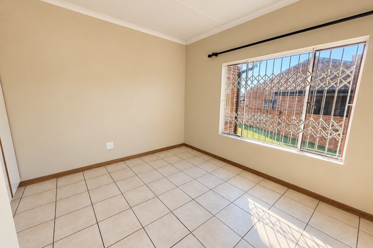 A bright, empty bedroom featuring neutral tiled flooring, clean walls, and a window fitted with a security gate.