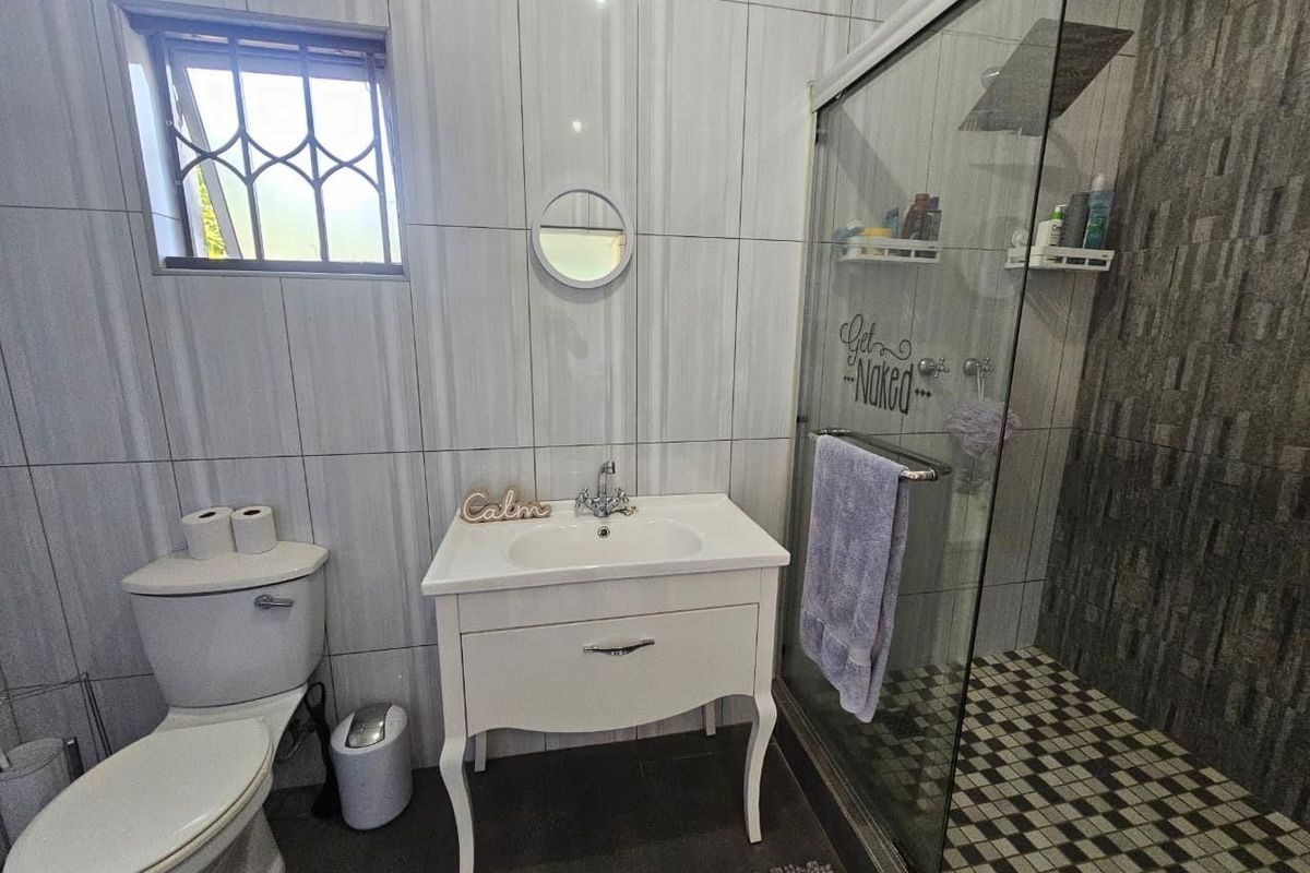 A functional bathroom featuring a vanity basin, toilet, and a glass-enclosed shower with modern tiled finishes and a window for natural light.