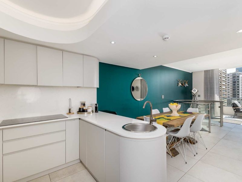 Modern open-plan kitchen and dining area featuring sleek cabinetry, stone countertops, integrated hob, and a glass balustrade overlooking the city.