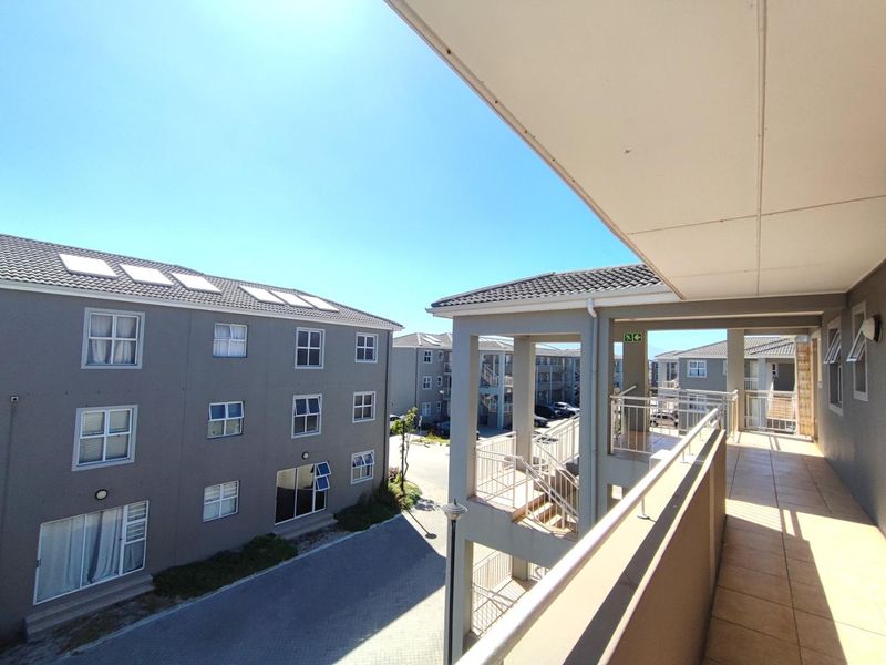 A covered balcony walkway overlooking the apartment complex courtyard and parking area, featuring tiled flooring and metal safety railings.
