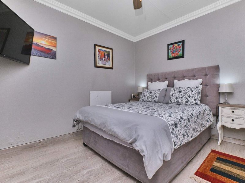 A well-maintained bedroom featuring laminate flooring, crown molding, and a ceiling fan, providing a comfortable and functional living space.