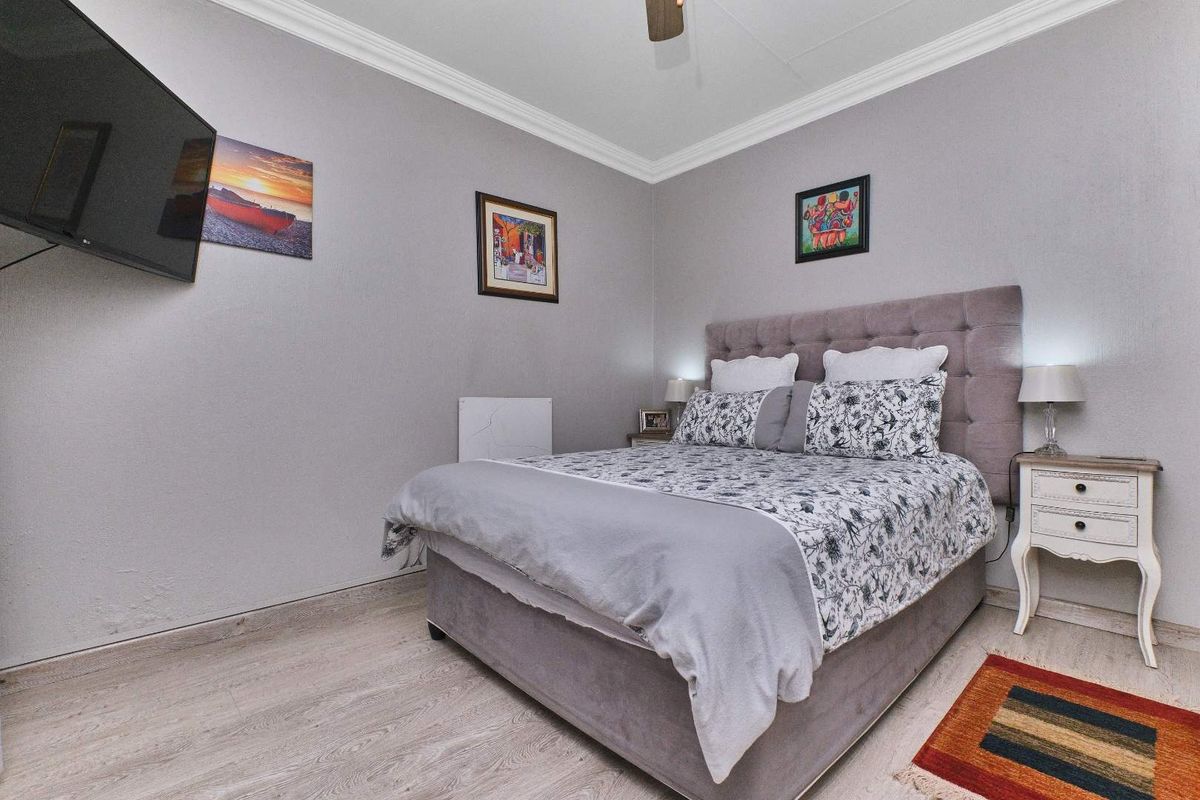 A well-maintained bedroom featuring laminate flooring, crown molding, and a ceiling fan, providing a comfortable and functional living space.