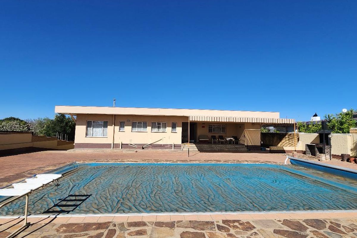 Spacious rear exterior featuring a large swimming pool with cover, paved patio area, and built-in outdoor braai, ideal for entertaining.