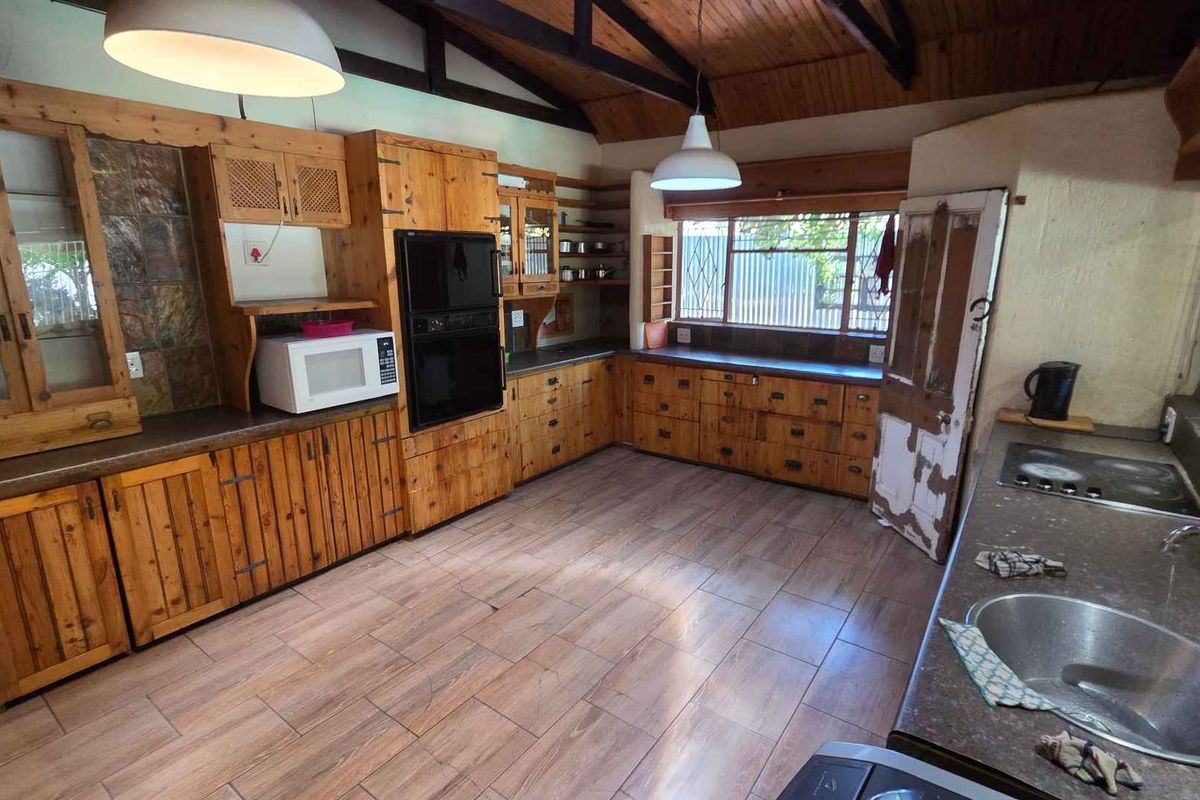 Spacious kitchen featuring rustic timber cabinetry, built-in oven, stone-look countertops, and vaulted timber ceilings with exposed beams.