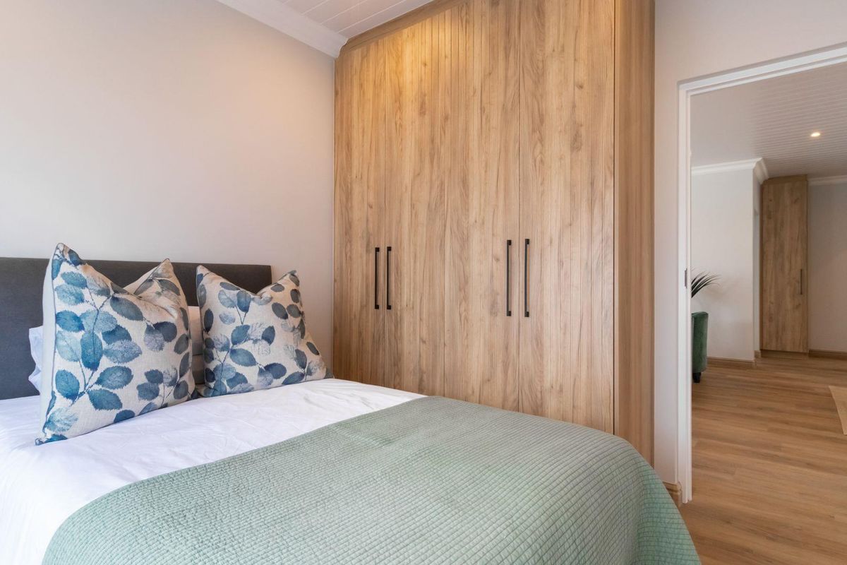 A well-appointed bedroom featuring modern wood-grain built-in cupboards and light-toned flooring, offering a clean and contemporary aesthetic.