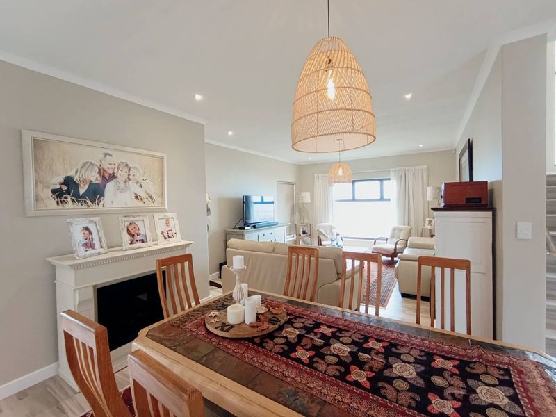 Open-plan living and dining area featuring a fireplace with mantelpiece, recessed downlights, pendant lighting, and light-toned laminate flooring.