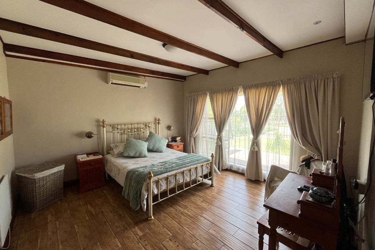 Spacious bedroom featuring exposed timber ceiling beams, wood-look tiled flooring, and a wall-mounted air conditioning unit with direct access to the garden.