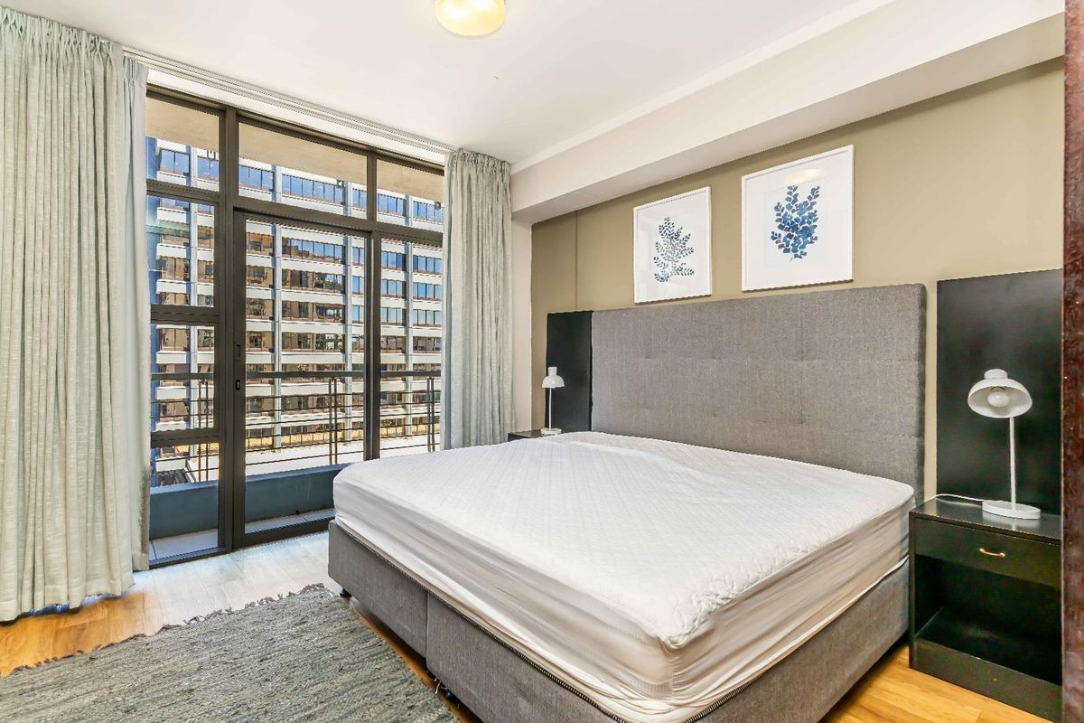 A well-lit bedroom featuring laminate flooring and a large glass sliding door providing access to an outdoor balcony area.