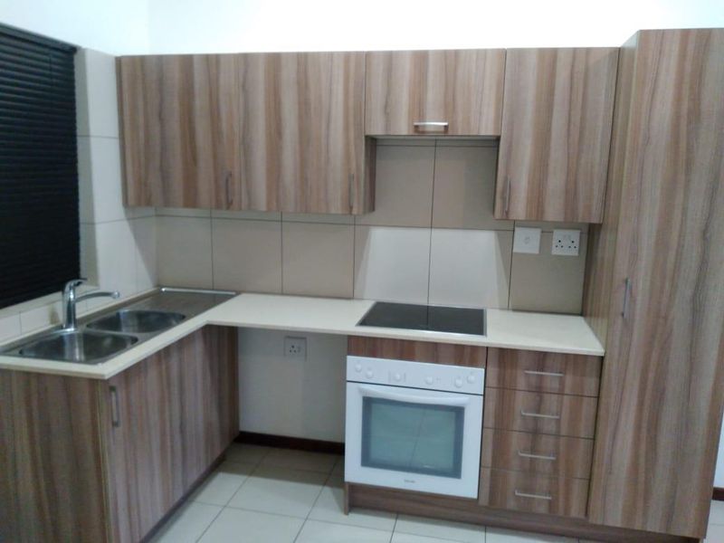 A clean, functional kitchen featuring wood-look laminate cabinetry, built-in oven, electric hob, and a double bowl sink with tiled splashback.