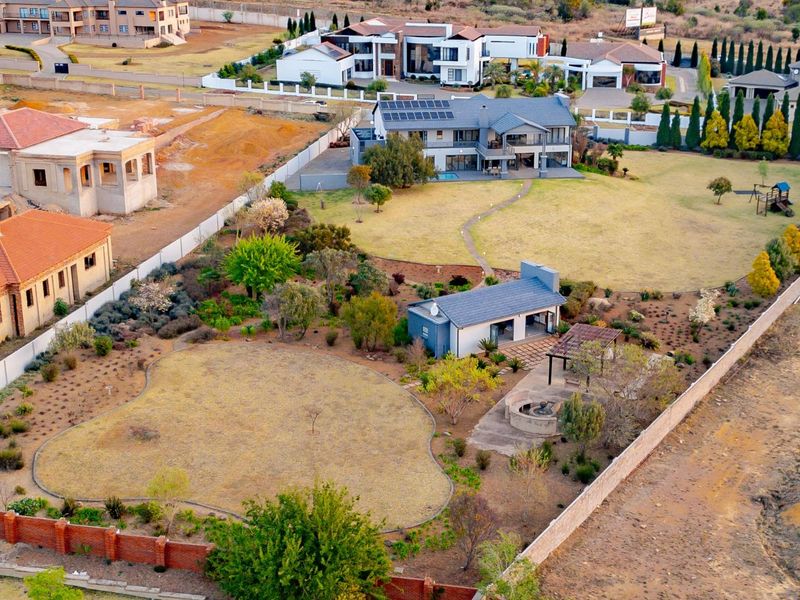 Aerial view of a large residential property featuring a main house with solar panels, a landscaped garden, swimming pool, and a detached outdoor entertainment area.