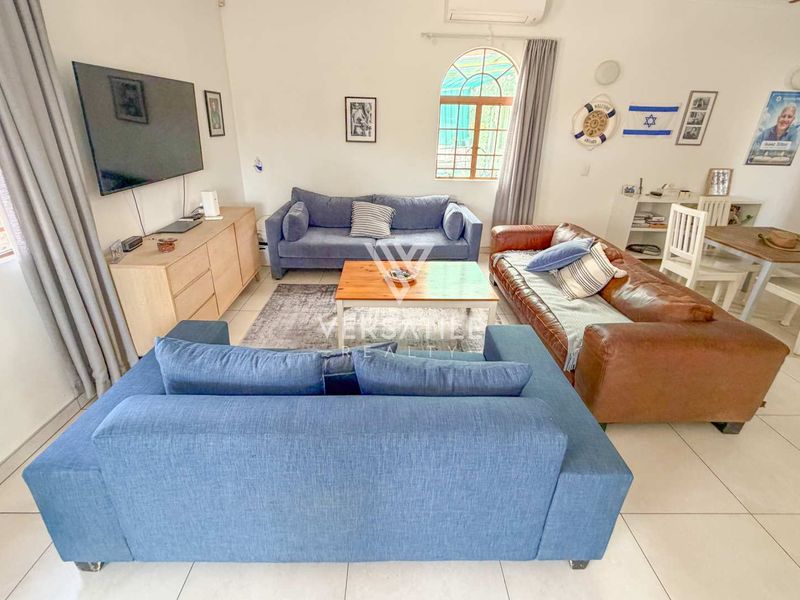 A bright and spacious living room featuring tiled flooring, an arched window, and a wall-mounted air conditioning unit.