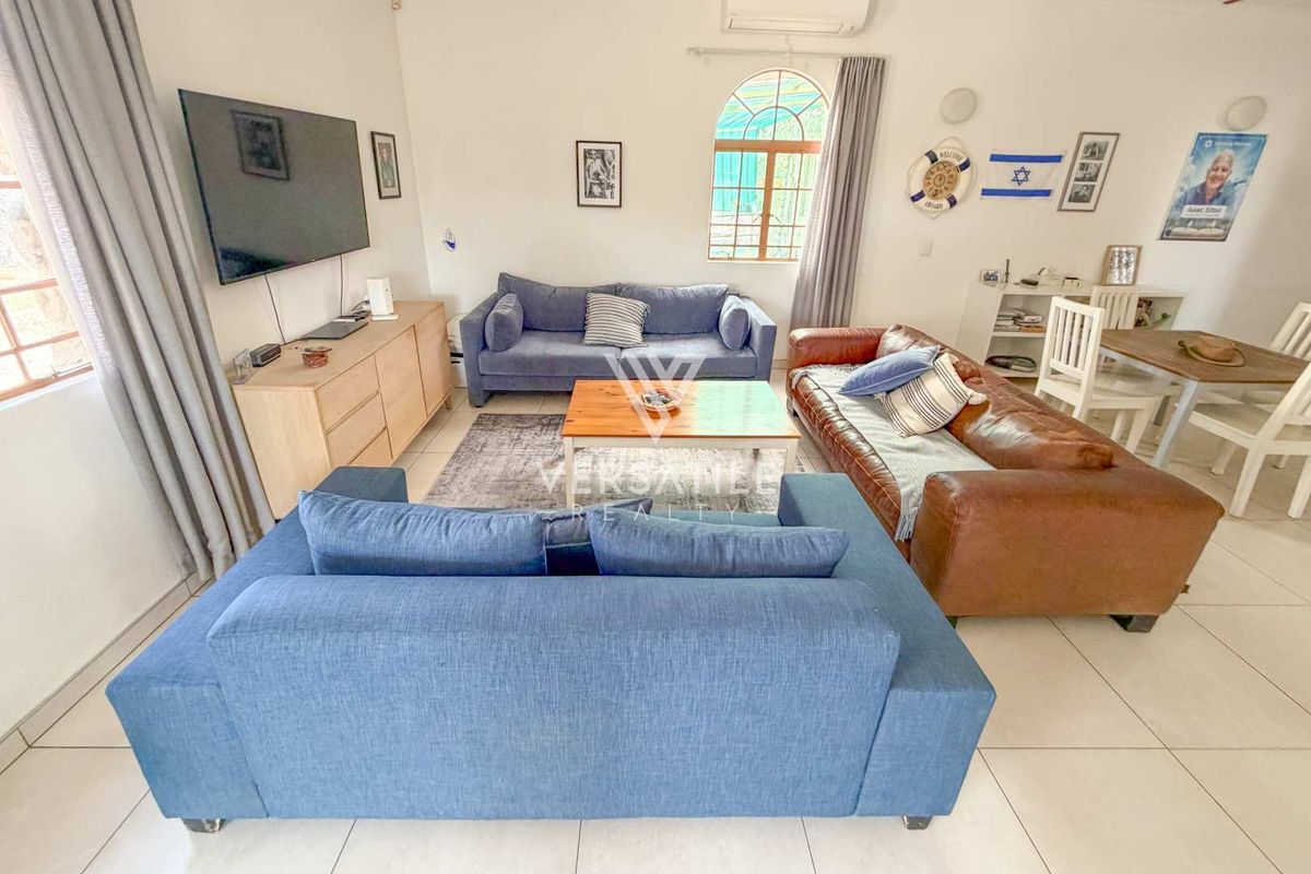 A bright and spacious living room featuring tiled flooring, an arched window, and a wall-mounted air conditioning unit.