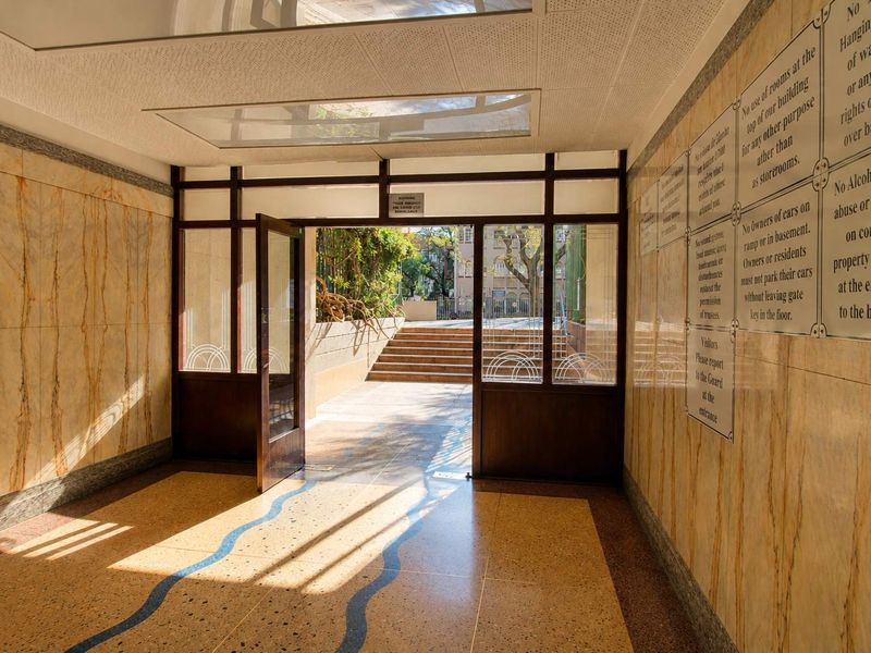 A well-maintained apartment building entrance lobby featuring classic marble wall cladding, terrazzo flooring with decorative inlay, and glass-panelled doors leading to the exterior.