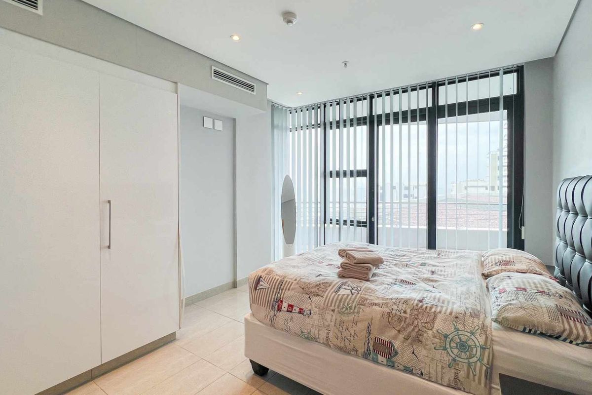 Modern bedroom featuring built-in floor-to-ceiling wardrobes, tiled flooring, ducted air conditioning, and large windows with vertical blinds offering natural light.