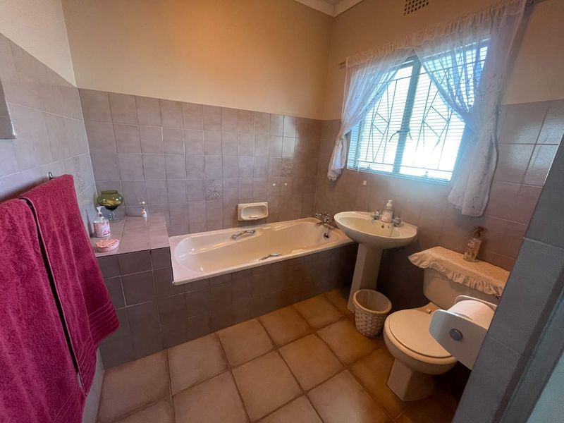A functional bathroom featuring a built-in bathtub, pedestal basin, and toilet, finished with neutral ceramic wall and floor tiles.