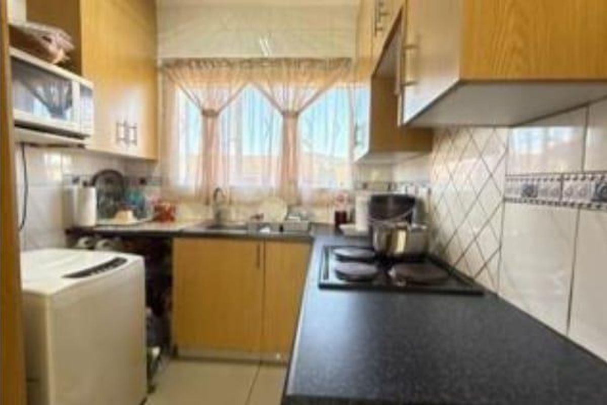 A functional kitchen featuring wood-finish cabinetry, a built-in electric hob, tiled splashbacks, and space for a washing machine.