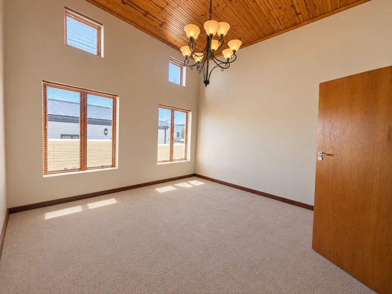 Spacious bedroom featuring high timber ceilings, large windows with natural light, and neutral carpeting, offering a blank canvas for personalization.