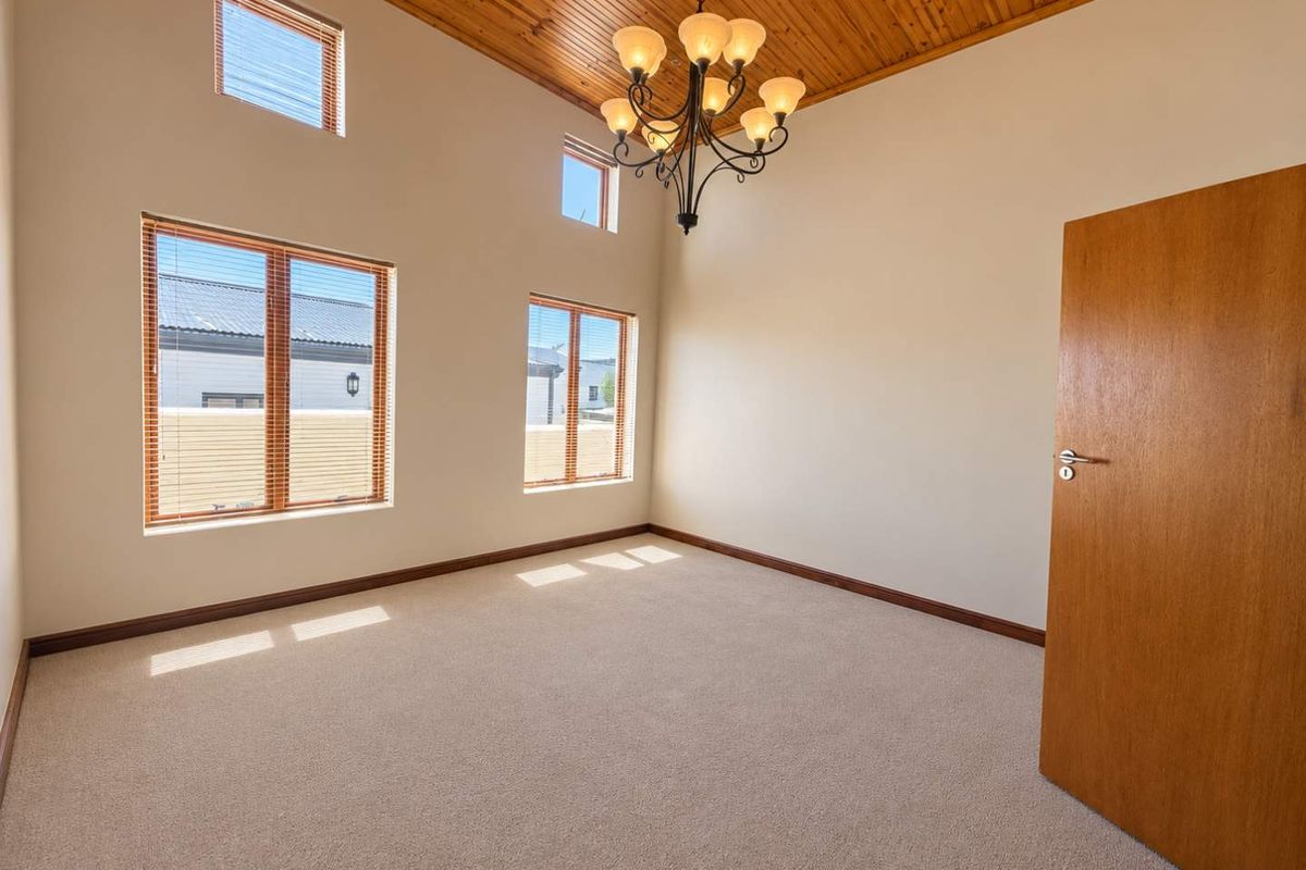 Spacious bedroom featuring high timber ceilings, large windows with natural light, and neutral carpeting, offering a blank canvas for personalization.