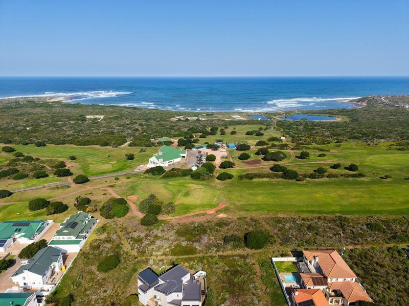An aerial view of a coastal residential area featuring a golf course, natural vegetation, and proximity to the ocean.