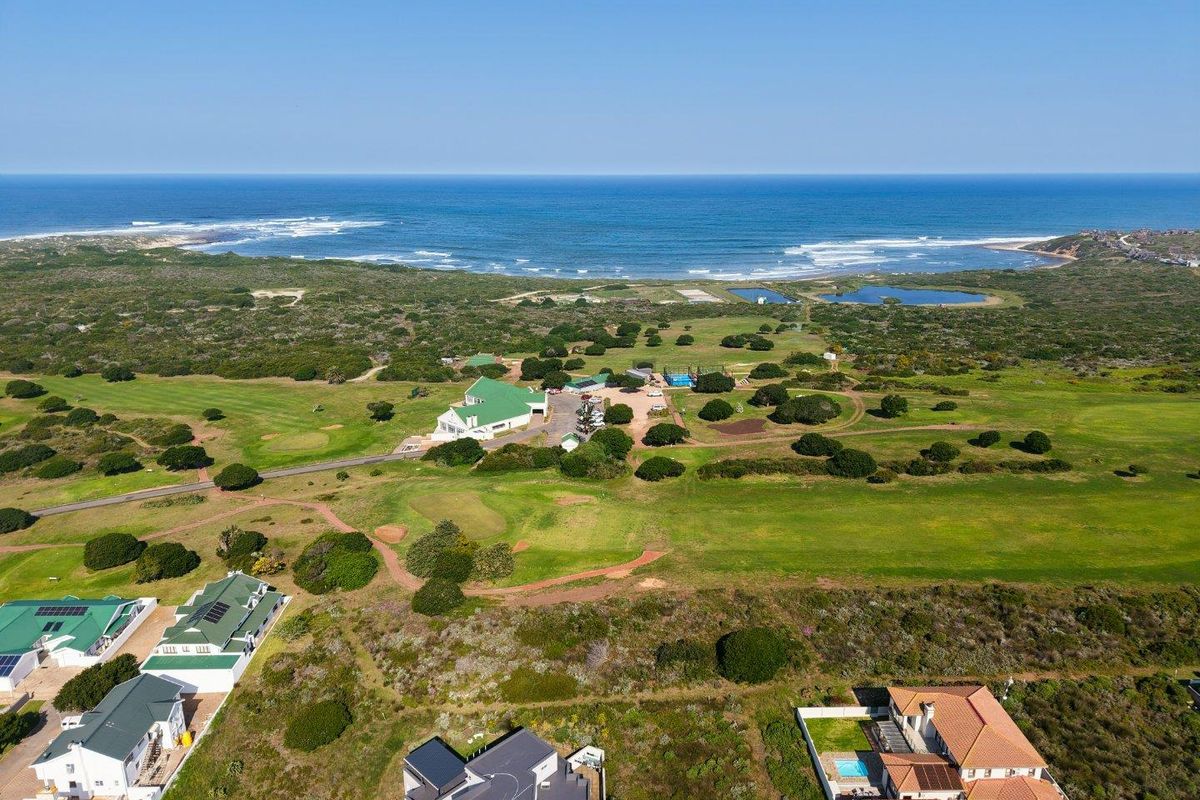 An aerial view of a coastal residential area featuring a golf course, natural vegetation, and proximity to the ocean.