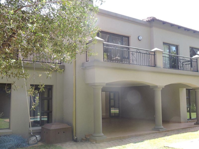 Rear elevation of the house featuring a covered patio area, an upper-level balcony with wrought iron railings, and large sliding glass doors.
