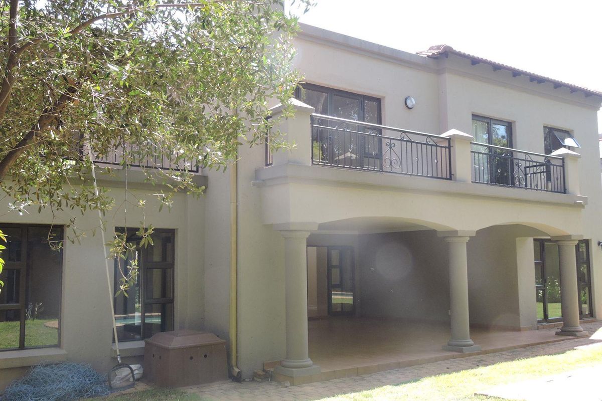 Rear elevation of the house featuring a covered patio area, an upper-level balcony with wrought iron railings, and large sliding glass doors.