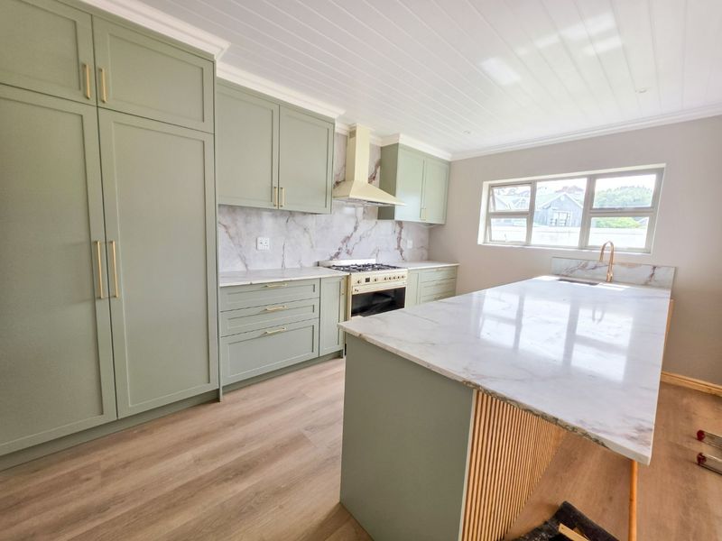 Modern kitchen featuring sage green shaker cabinetry, marble-look stone countertops, a central island, and high-end brass fixtures with integrated appliances.