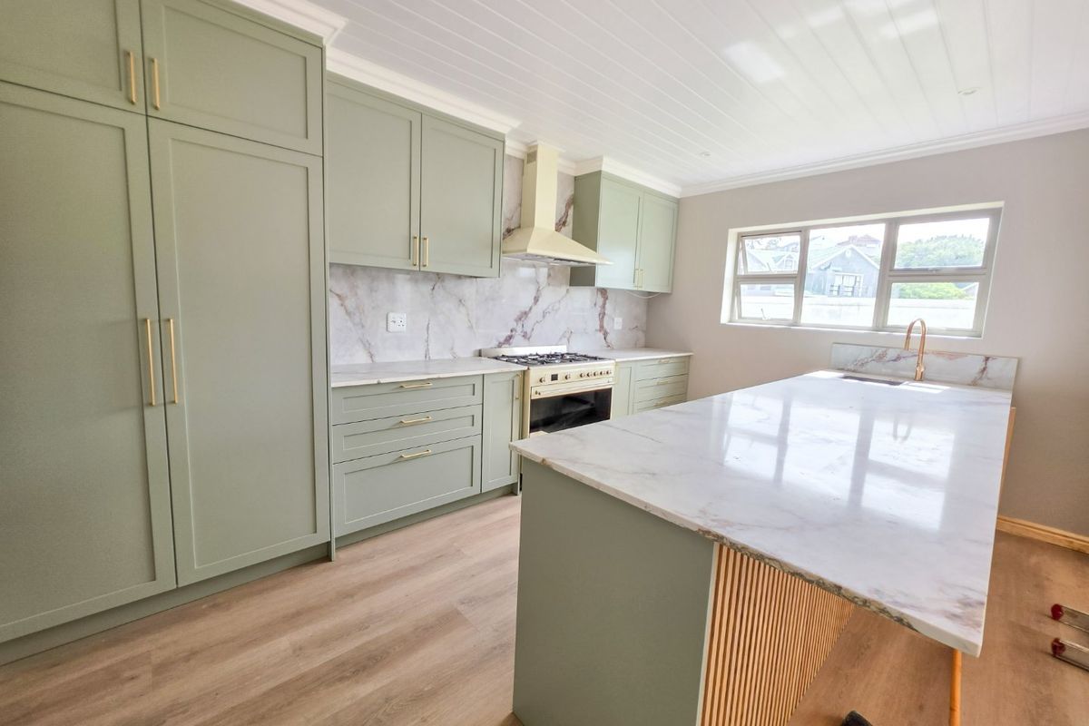 Modern kitchen featuring sage green shaker cabinetry, marble-look stone countertops, a central island, and high-end brass fixtures with integrated appliances.