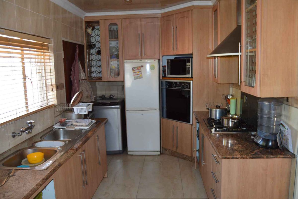 Functional kitchen featuring wood-veneer cabinetry, granite countertops, built-in oven, gas hob, extractor fan, and double stainless steel sink.