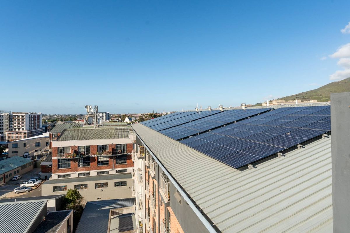 Aerial view of the apartment building roof featuring a large array of installed solar panels and metal roofing.