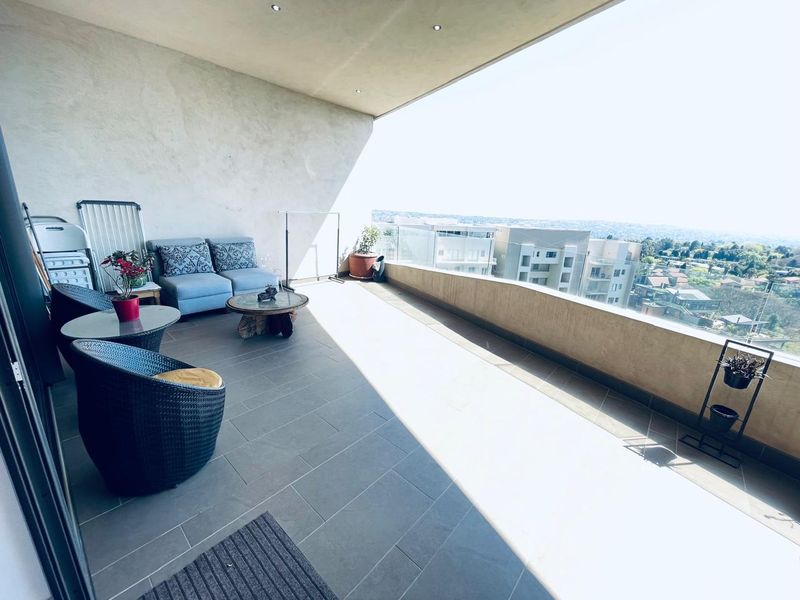 Spacious covered balcony featuring tiled flooring, recessed lighting, and a modern glass balustrade with expansive urban views.