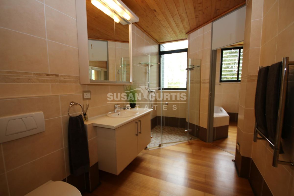 Modern bathroom featuring a vanity, glass shower enclosure, timber ceiling, and tiled finishes, with a separate area containing a bathtub.