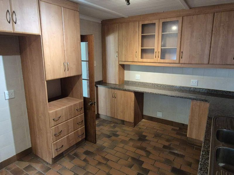 A functional kitchen featuring wood-look laminate cabinetry, granite countertops, a double basin sink, and durable brick flooring.