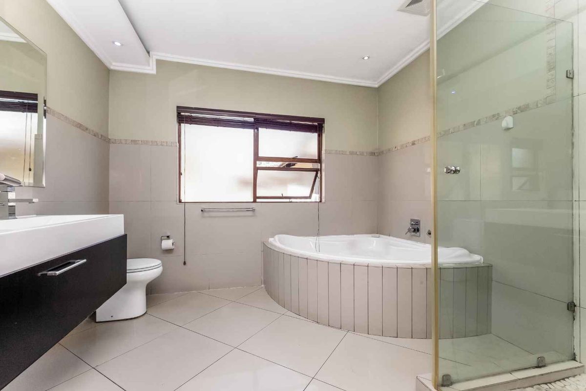 Modern bathroom featuring a corner soaking tub, a glass-enclosed walk-in shower, a wall-mounted vanity, and neutral floor-to-ceiling tiling.