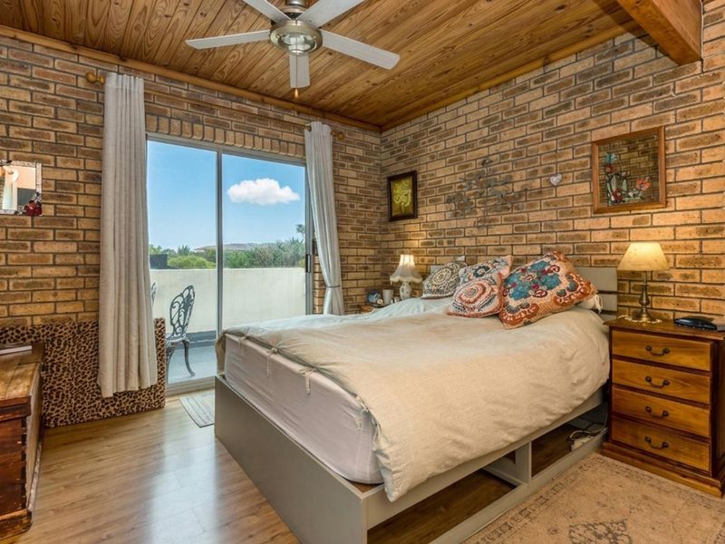 A bedroom featuring exposed brick walls, a timber-clad ceiling with a fan, and a sliding glass door providing access to an outdoor balcony.