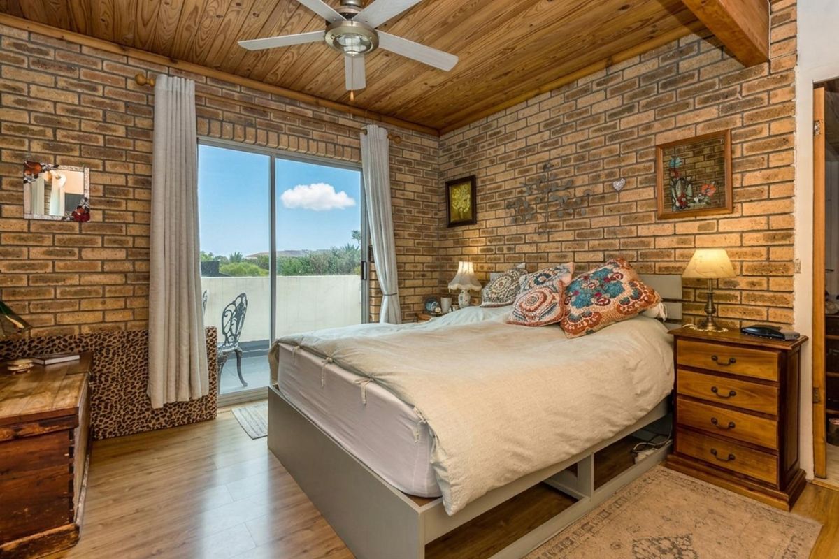 A bedroom featuring exposed brick walls, a timber-clad ceiling with a fan, and a sliding glass door providing access to an outdoor balcony.