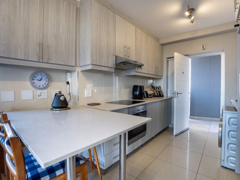 Modern kitchen featuring light wood-grain cabinetry, stone countertops, integrated appliances, and a convenient breakfast bar, with tiled flooring throughout.