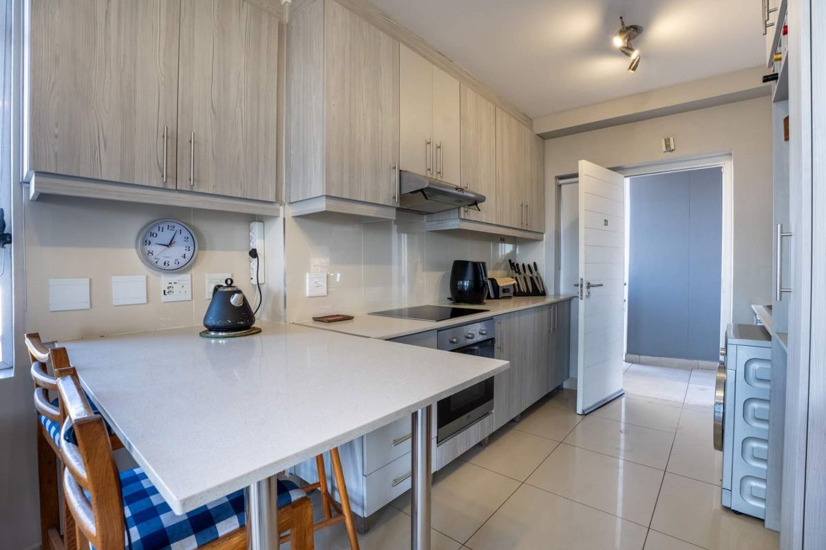 Modern kitchen featuring light wood-grain cabinetry, stone countertops, integrated appliances, and a convenient breakfast bar, with tiled flooring throughout.