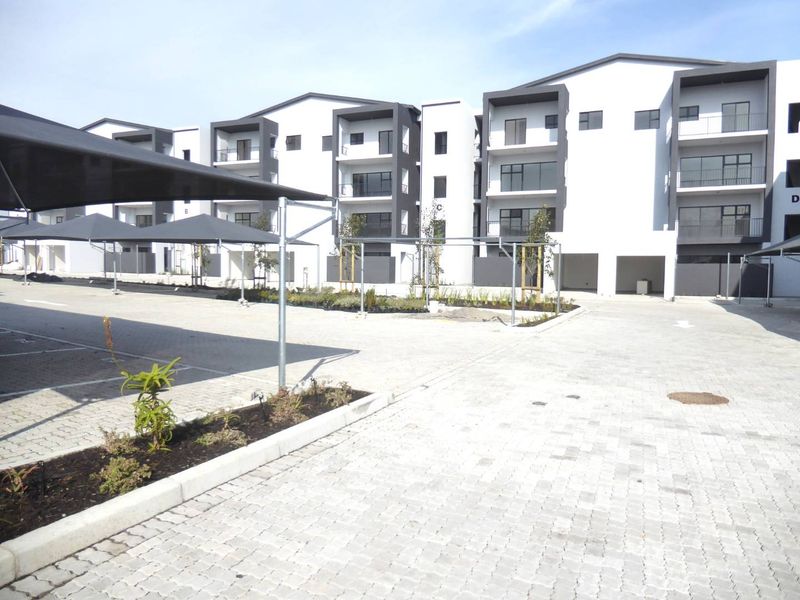 Modern multi-story apartment complex featuring paved parking areas with shade cloth carports and landscaped garden beds.