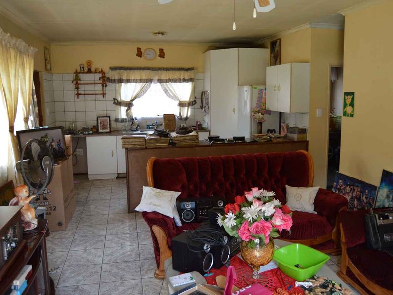 Open plan living and kitchen area featuring tiled flooring, built-in cabinetry, and a functional kitchen layout in need of cosmetic updates.