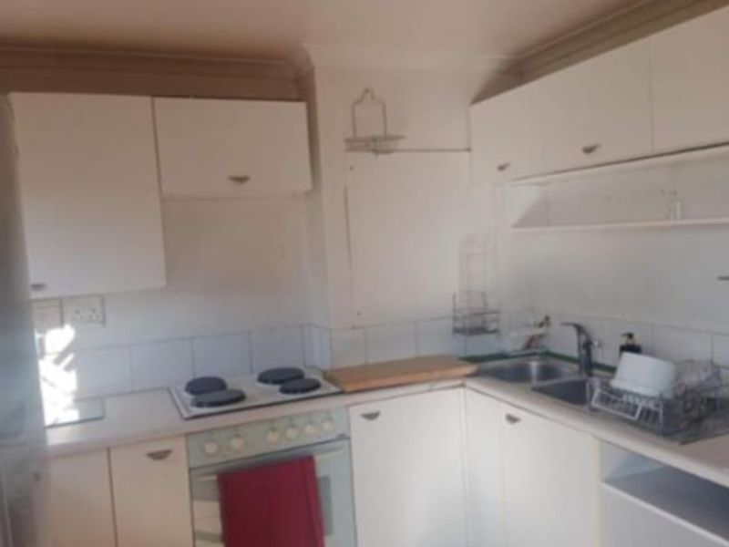 A compact kitchen featuring white built-in cabinetry, an electric hob, an oven, and a double sink with a tiled backsplash.